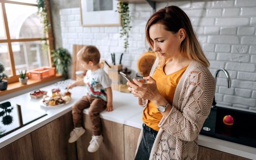 A mother looking at her phone while looking after her child. Photo iStock