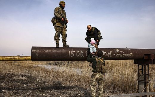 Ukrainian serviceman hands over the baby of a displaced family to help to cross a river. Photo AFP, Ronaldo Schemidt
