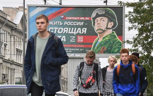 Young men walk in front of a billboard promoting contract army service with an image of a serviceman and the slogan reading "Serving Russia is a real job" in Saint Petersburg. Photo AFP, Olga Maltseva