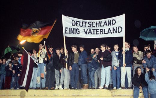 Germans stand on the Berlin Wall to celebrate its demolition. The banner reads: "Germany, only Fatherland". Photo EPA

