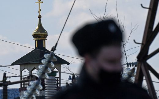 Russian police officer patrols outside the territory of the penal colony N2 with an Orthodox church. Photo AFP, Kirill Kuryavtsev