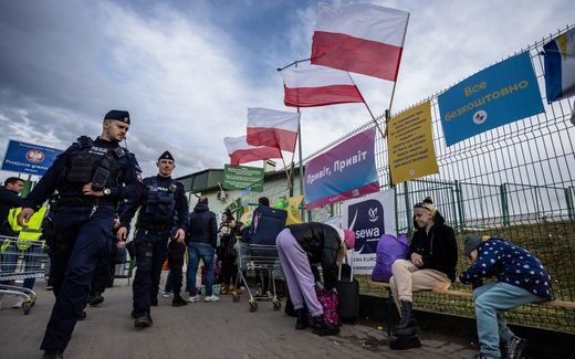 Polish Police officers walk past refugees from Ukraine resting at the Polish/Ukrainian border crossing in Medyka. Photo AFP, Wojtek Radwanski