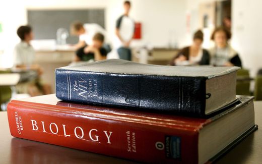 A bible on top of a biology text book while students study in the background. Photo EPA, Justin Lane