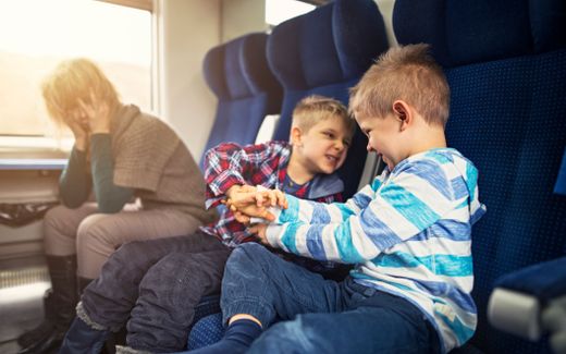 Two little boys are embarrassing their mother on a train ride. Photo iStock