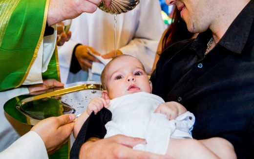 A father holds his child as it is baptised. Photo iStock