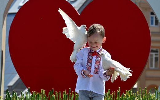 A boy wearing a Vyshyvanka, a traditional Ukrainian embroidered blouse, holds pigeons as he poses for his mother at Independence Square in Kyiv. Photo AFP, Sergei Supinsky
