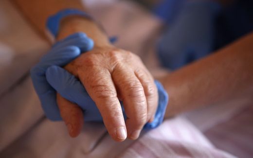 A nurse wearing protective gloves holds the hand of a patient in the palliative care unit of a hospital. Photo AFP, Pascal Pochard-Casabianca