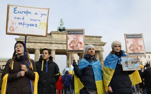 Protestor wrapped in Ukrainian flags hold placards reading "Stop Putler" and "Europe, do you need more refugees?" stand in front of Brandenburg Gate in Berlin to demonstrate for peace in Ukraine. Photo AFP, Odd Andersen
