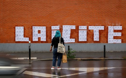 A feminist activist looks at posters of a drawing by French cartoonist Charb to read "laïcité", secularism, in Montreuil, on October 20, 2020. Photo AFP
